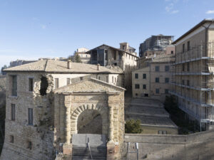 Borgo storico con edifici in pietra, porta ad arco e strutture in ristrutturazione con impalcature.