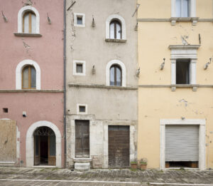 Facciate con crepe di tre edifici adiacenti color rosa, beige e giallo con porte e finestre.