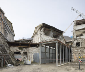 Edificio in rovina con impalcature metalliche e gru da cantiere nello sfondo.