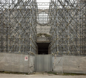 Ponteggi metallici e recinzione con cartello di divieto davanti a edificio in pietra in restauro.