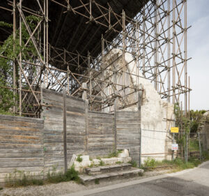 Resti di edificio antico con impalcature metalliche e recinzione in legno per restauro.
