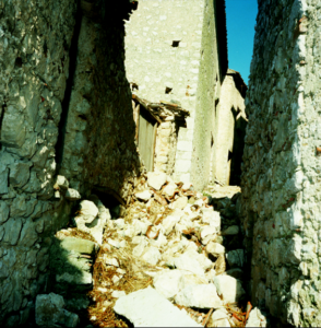 Viottolo stretto in pietra con macerie davanti a edifici antichi sotto cielo sereno.