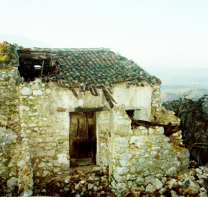 Casa in pietra in rovina con tetto in tegole danneggiato in paesaggio collinare.