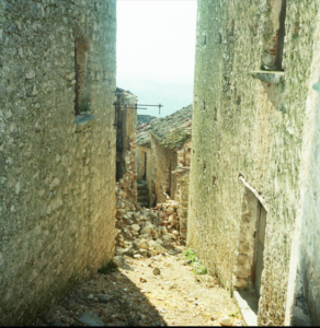 Vicoli stretti tra edifici in pietra con detriti e macerie a ostruire il passaggio.