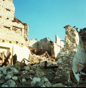 Rovine di edificio in pietra parzialmente crollato con detriti sotto cielo sereno.