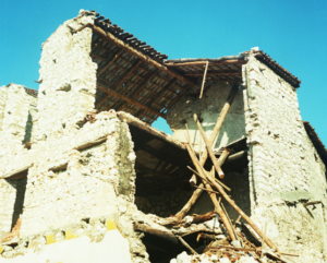 Ruderi di edificio in pietra con tetto crollato e travi di legno esposte sotto cielo sereno