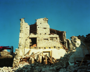 Rovine di edificio in pietra parzialmente crollato con travi di legno e detriti sotto cielo sereno.