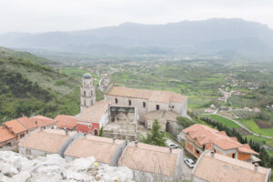Borgo con tetti in tegole rosse e chiesa con campanile a cupola circondato da campi e colline.