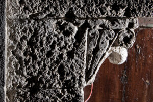 Capitello in pietra scolpita con dettagli decorativi su sfondo di porta in legno.