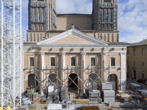 Facciata di edificio storico in mattoni con colonne, archi e torri in restauro con impalcature e gru.