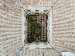 Cortile interno quadrato con casse impilate, piante e tetto in tegole con scritta Filippo Marchetti.
