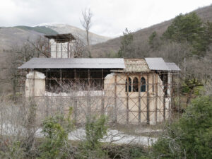 Vecchio edificio in rovina con impalcature in un paesaggio montano invernale con alberi spogli.