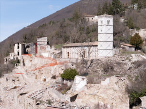 Rovine di edifici storici su collina con torre bianca intatta e vegetazione invernale.