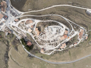 Veduta aerea di borgo rurale con case, strade curvilinee e aree in demolizione circostanti campi.