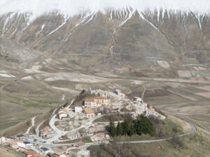 Borgo su altura con case, strade tortuose e montagne con cime innevate sullo sfondo.