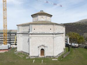 Edificio ottagonale storico in pietra chiara con tetto a cupola in restauro, circondato da prato.