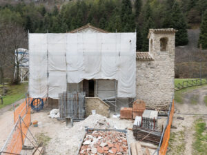 Restauro di edificio in pietra con impalcature e materiali edili in area verde con alberi.