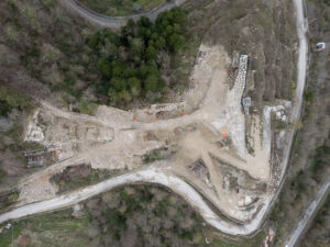 Veduta aerea di area rurale con vecchie strutture in rovina, strade sterrate e operai in arancione.