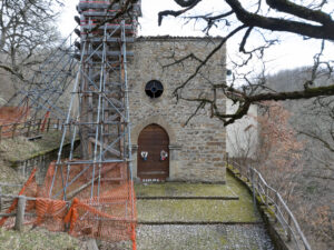 Cappella in pietra con porta ad arco e rosone, impalcature e reti arancioni per restauro esterno.