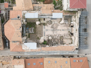 Sito archeologico con resti di pavimentazione antica, strutture parziali e impalcature metalliche.
