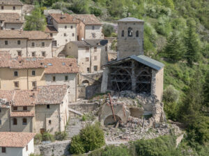Villaggio con case in pietra e tetti in tegole, struttura storica in rovina con impalcature.