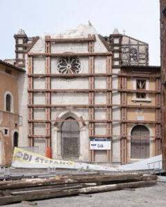 Facciata di edificio storico danneggiato con struttura metallica di sostegno e materiali da cantiere.
