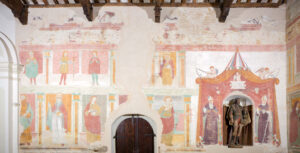 Affresco con figure religiose e statua lignea in nicchia su parete di edificio storico.