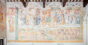 Affresco religioso con santi e angeli in alto, demoni e dannati in basso, in edificio con travi in legno.