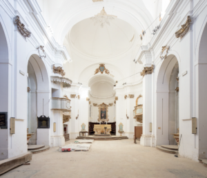 Interno di chiesa con soffitto a volta, pareti bianche, altare ornato e pavimento con materiali da costruzione.