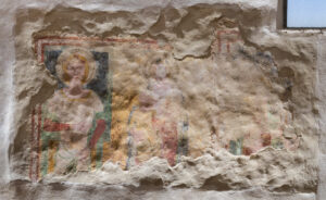 Affresco deteriorato su parete con figure sacre e aureole parzialmente visibili.