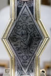 Incisione su metallo di figura religiosa con aureola circondata da cherubini alati su cornice dorata.