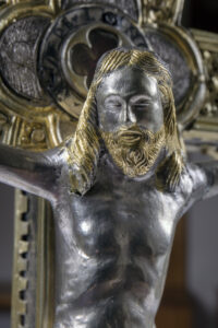 Cristo crocifisso in metallo con capelli e barba dorati in stile dettagliato.