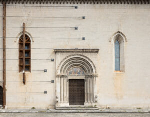 Facciata con portale decorato da archi concentrici, affresco, finestre gotiche e rinforzi metallici.