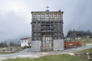 Edificio in pietra con croce in ristrutturazione circondato da impalcature in area rurale.